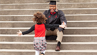 A University of Alabama graduate wearing his cap and gown is about to hug his daughter.